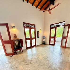 Une pièce spacieuse avec un plafond haut, des portes en bois ornées de panneaux de verre décoratifs, un ventilateur de plafond et un distributeur d’eau.