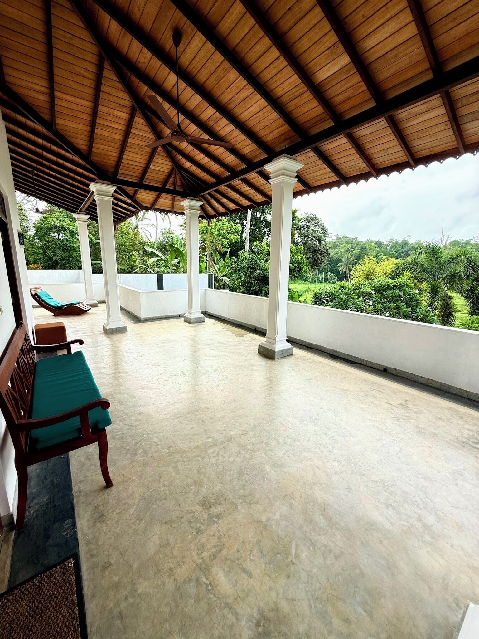 A covered outdoor area with a wooden ceiling, white columns, and a bench with a green cushion.