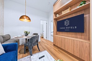 A modern room with a dining table set, a blue sofa, a grey armchair, a wooden cabinet, and a mounted TV displaying 'Casa Hotels Toronto'. - The Gerrard Brand New CN Tower Home Base (Toronto)