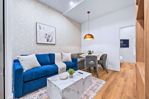 A modern living room with a blue sofa, a marble coffee table, a pendant light, and a dining area with a table and chairs. - The Gerrard Brand New Fifa Event Stay (Toronto)