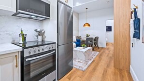 A modern kitchen with stainless steel appliances, a marble countertop, and a dining area with a wooden floor and a hanging pendant light. - The Gerrard Brand New CN Tower Home Base (Toronto)