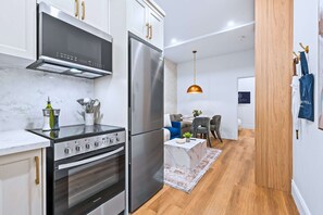 A modern kitchen with stainless steel appliances, a marble countertop, and a dining area with a wooden floor and a hanging pendant light. - The Gerrard Brand New Fifa Event Stay (Toronto)
