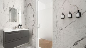 A modern bathroom with a marble wall, a vanity with a mirror, and two bottles of shampoo.