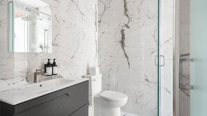 Ein Badezimmer mit Marmorwand, einer Duschkabine aus Glas, einer weißen Toilette und einem Waschtisch mit Spiegel.