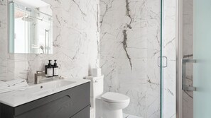 A bathroom with a marble wall, a glass shower enclosure, a white toilet, and a vanity with a mirror.