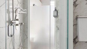 Ein modernes Badezimmer mit Duschkabine aus Glas, einer Handbrause und einer zusätzlichen Duscharmatur, sowie einer Shampoo-Flasche.