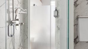Ein modernes Badezimmer mit Duschkabine aus Glas, einer Handbrause und einer zusätzlichen Duscharmatur, sowie einer Shampoo-Flasche.