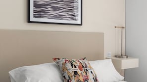 Ein Hotelzimmer mit Bett, einem Kissen mit farbigem Muster, einem gerahmten Kunstwerk über dem Bett und einem Nachttisch mit Lampe.