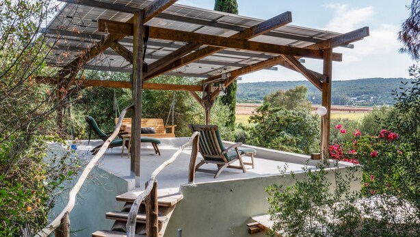 Zona relax all'aperto, riparata da una pergola, con mobili in legno e vista sulla campagna.