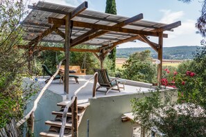 A covered outdoor seating area with a pergola, wooden furniture, and a view of the countryside. - Casa Hada: Calm, Nature and You (El Soto)