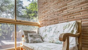 Una panca di legno con rivestimento floreale, un muro in mattoni e un'ampia finestra con vista su uno spazio esterno.