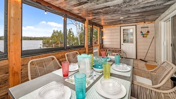 A rustic dining area with a table set for four, large windows, and a view of a lake. - Pôr do Sol  Whitelake Waterfront  Group  Getaway (White Lake)