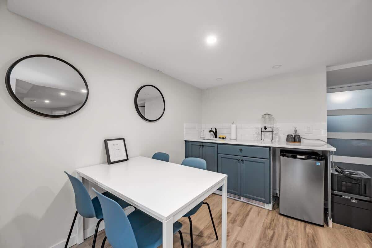 Una cocina compacta con muebles blancos, una encimera blanca, un lavavajillas de acero inoxidable y un espejo redondo en la pared.