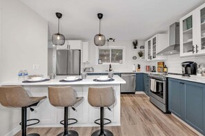 A modern kitchen with a central island, bar stools, stainless steel appliances, and pendant lighting.
