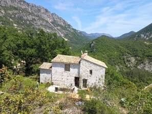 Ein Haus aus Stein mit Ziegeldach, umgeben von viel Grün und Bergen.