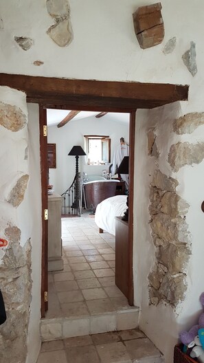 Ein schmaler Flur führt zu einem Schlafzimmer mit einer großen Badewanne, einem hölzernen Türrahmen und einem gefliesten Boden.