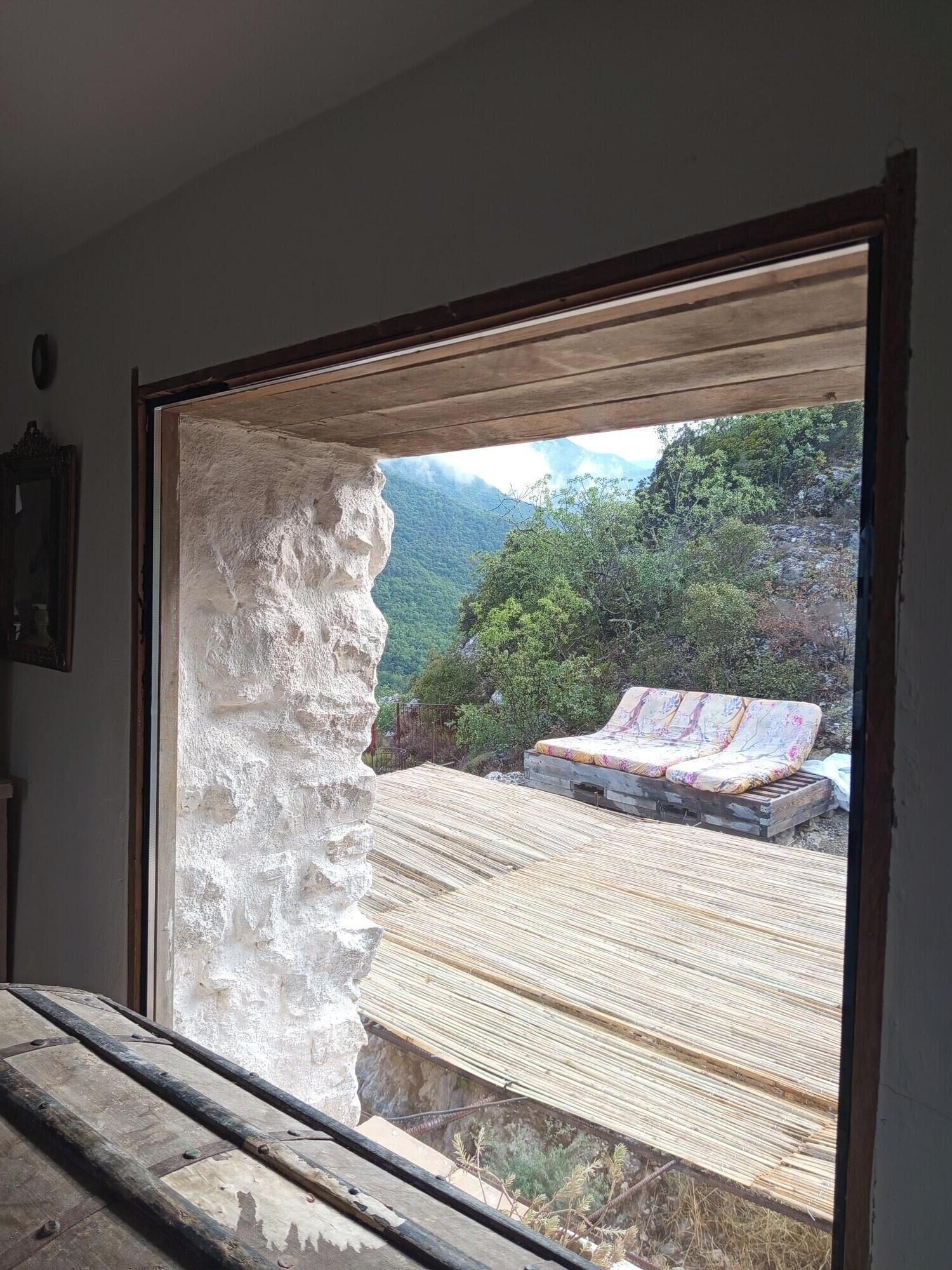 A room with a large window, a wooden bench, and a view of a mountainous landscape.