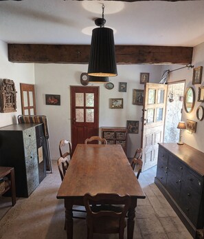A rustic dining area with a wooden table and chairs, a hanging light fixture, and a wooden cabinet with drawers. - Nature refuge in the Estéron valley, small authentic sheepfold, bohemian spirit (Sigale)