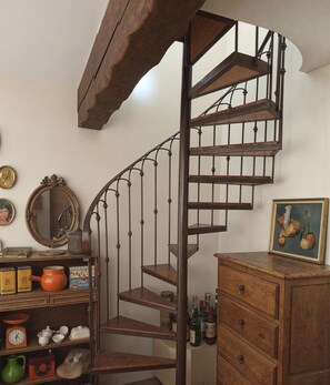 A spiral staircase with wooden steps and metal balusters, a vintage mirror, and a cabinet with drawers and a framed picture. - Nature refuge in the Estéron valley, small authentic sheepfold, bohemian spirit (Sigale)