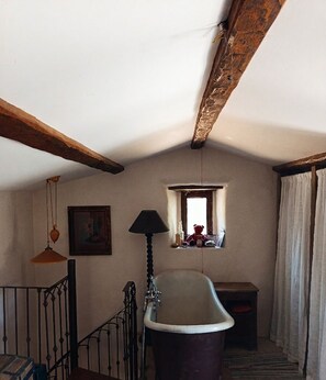 Una habitación con bañera, ventana con vistas, lámpara colgante y un cuadro en la pared.