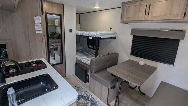 Interior compacto de una caravana con kitchenette, una litera y un pequeño comedor.