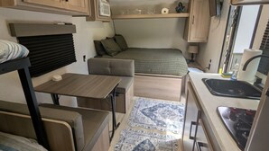 Interior compacto de una autocaravana con kitchenette, cama y zona de comedor.