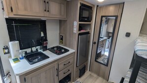 Una cocina compacta para vehículo recreativo, con lavamanos, estufa, microondas y refrigerador.