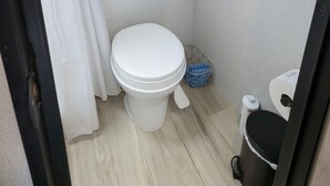 Un baño con inodoro, una toalla colgada, un espejo y un cubo de basura.