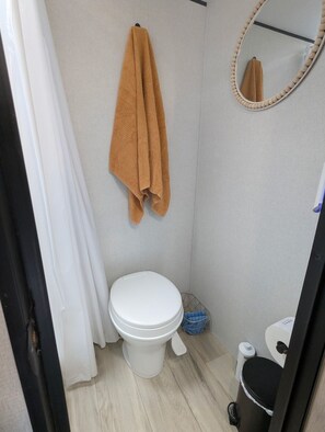 A bathroom with a toilet, a hanging towel, a mirror, and a trash bin.