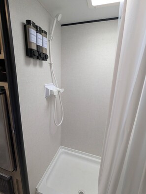 A shower with a handheld showerhead, a wall-mounted faucet, and three bottles of shampoo, conditioner, and body wash.