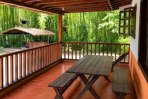Un espace extérieur abrité, doté d’une table et de bancs en bois, entouré d’une clôture en bambou et agrémenté d’un barbecue en briques.