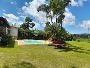Un jardin avec une piscine, un banc rouge et une maison.