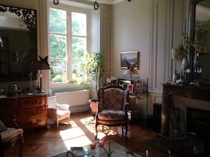 Een kamer met een houten vloer, een stoel, een dressoir, een tafel, een raam en een spiegel.