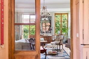 A room with a large mirror, wooden furniture, a chandelier, and a view of greenery outside.