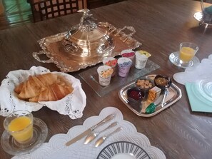 Disposição para o café da manhã com croissants, potinhos de iogurte e uma bandeja de prata com geleias e doces.