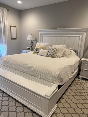 A neatly made bed with a white headboard, a bedside table with a lamp, and a patterned carpet. - Spacious 4 bedroom Retreat with Beautiful Pool in Glendale. Sleeps 10-12 (Glendale)
