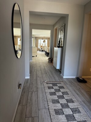 Un pasillo con piso de madera, un tapete estampado, un espejo y una zona de comedor al fondo.