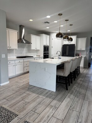 A modern kitchen with white cabinetry, a central island, and a wood-patterned floor. - Spacious 4 bedroom 4 bath Retreat with Beautiful Pool in Glendale. Sleeps 10-12 (Glendale)