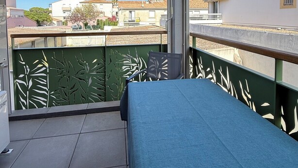 Een balkon met een blauwe bank, een groen sierhek en uitzicht op gebouwen en bomen.