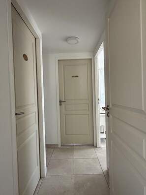 A hallway with a closed door labeled 'DOUGLAS,' tiled flooring, and white walls. - T2 avec terrasse, parking et cellier | La Roselière Le Grau-du-Roi (Le Grau-du-Roi)