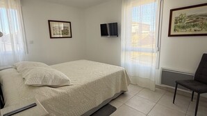 Een slaapkamer met een bed, een stoel, een televisie en twee foto's in lijsten aan de muur.