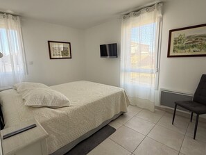 A bedroom with a bed, a chair, a TV, and two framed pictures on the wall. - T2 avec terrasse, parking et cellier | La Roselière Le Grau-du-Roi (Le Grau-du-Roi)