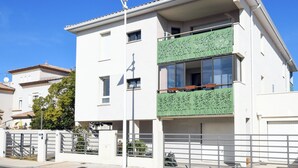 Een modern, tweelaags gebouw met een witte gevel, een groen balkon met decoratieve panelen en een metalen poort.