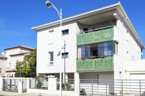 A modern two-story building with a white facade, a green balcony with decorative panels, and a metal gate. - T2 avec terrasse, parking et cellier | La Roselière Le Grau-du-Roi (Le Grau-du-Roi)