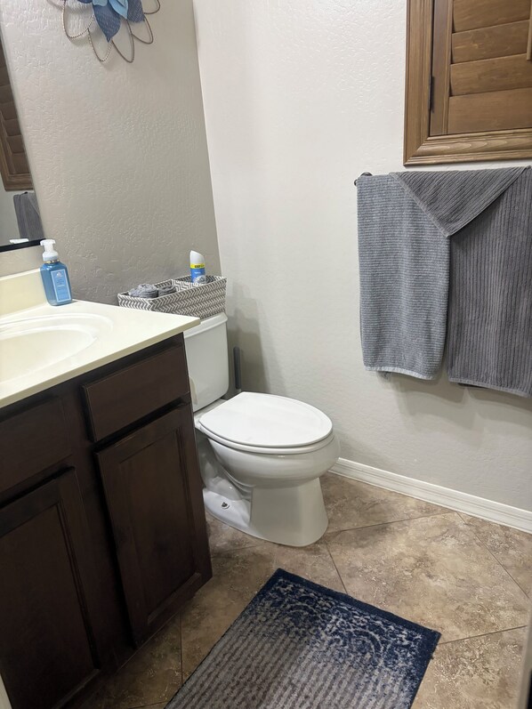 A bathroom with a white toilet, dark wooden cabinets, a white sink, a blue bottle, and a gray towel on the wall.