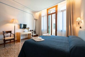Een hotelkamer met een bed, bureau, stoel, televisie en gordijnen.