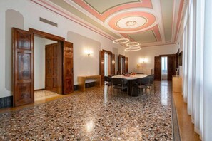 Een ruime kamer met een terrazzovloer, houten deuren, een ronde eettafel met stoelen en een plafond met een cirkelvormig ontwerp.