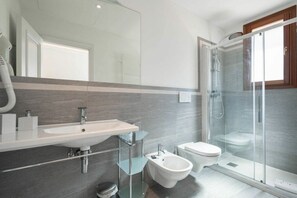 Een moderne badkamer met een glazen douchecabine, een hygiëneschuiver en een toilet.