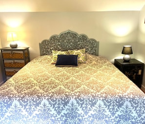 Een bed met een bedsprei met patroon, een decoratief hoofdbord en twee nachtkastjes met lampen.
