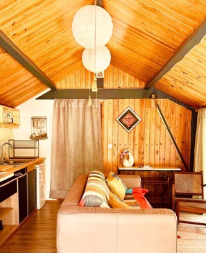 Una habitación acogedora con techo de madera, un sofá, una mesa de comedor y una lámpara colgante.